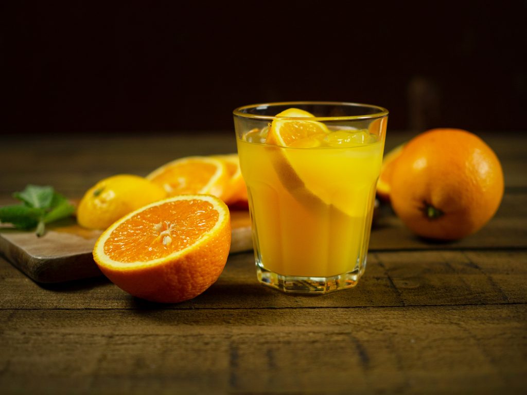 An aesthetic shot of a transparent glass filled with orange juice, rich in vitamin C, with slices of orange scattered nearby.