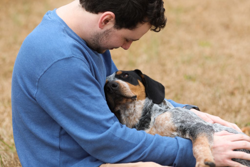 A man cuddling and smiling at his pet dog outdoors.