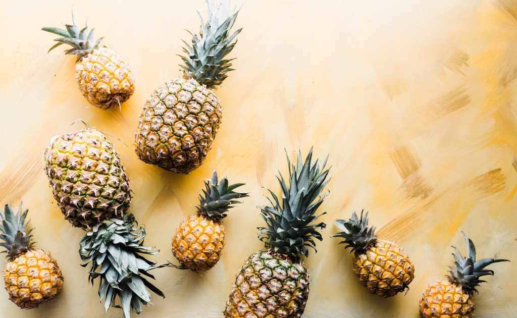 Pineapples of various shapes scattered on the floor, illustrating how this tropical fruit can help improve issues like bloating and swelling.