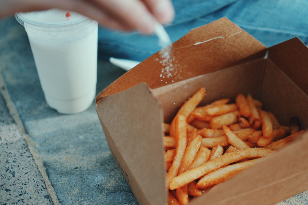 A close-up shot of a box filled with French fries being sprinkled with salt, highlighting how more salt can make you feel bloated.
