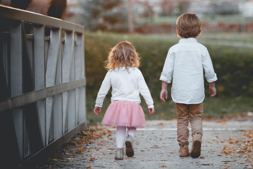 A cute photograph of two kids, a boy and a girl, strolling outdoors, signifying how a quick walk around the block can reduce stress