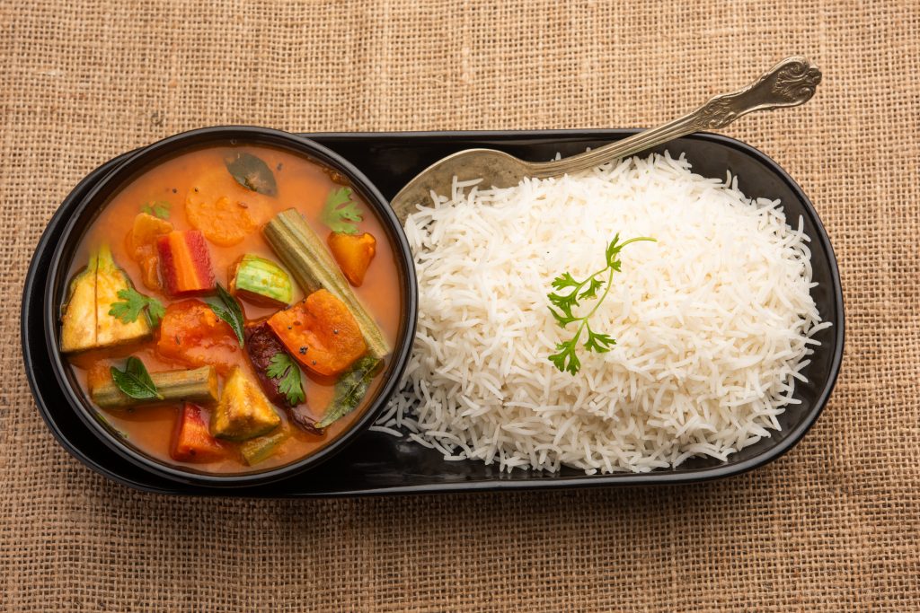 An elegant display of a plate of long-grain rice with a bowl of delicious sambar.