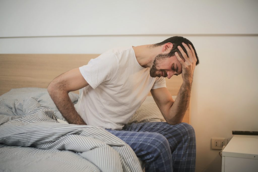 A man, seemingly suffering from a sleep disorder, sitting distraught on his bed.