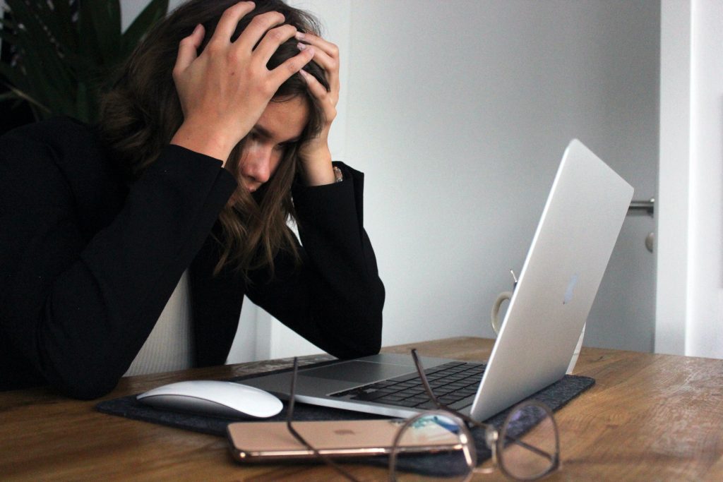 A young working woman using a computer, appearing distraught and stressed.