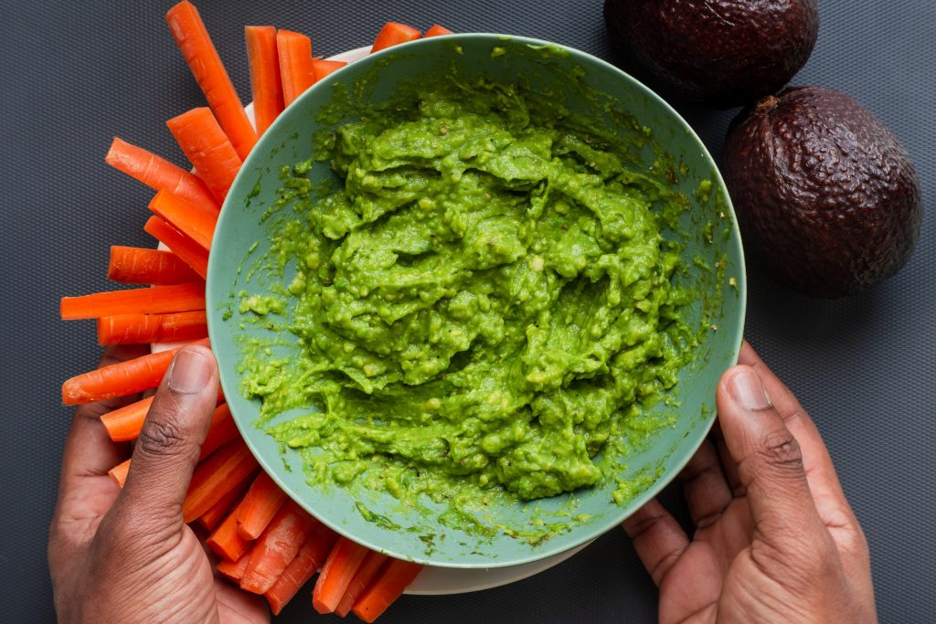 Low-cal, freshly cut carrots arranged on a plate with a green yogurt dip in a bowl.