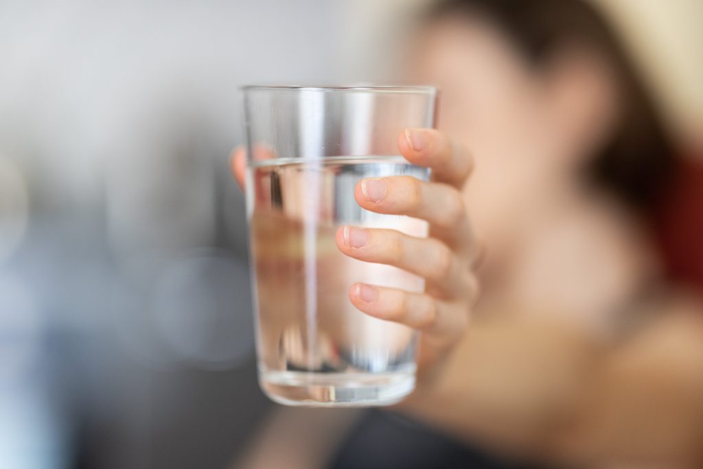 A close-up shot of a glass filled with water, held by a woman's hand.