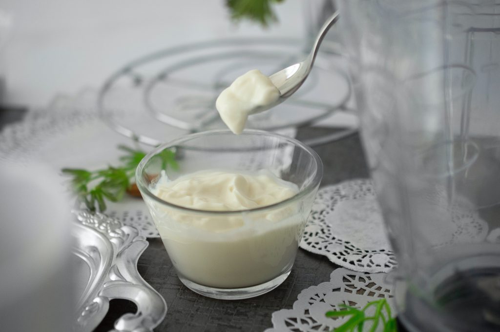 Hung curd being scooped with a steel spoon from a glass bowl.