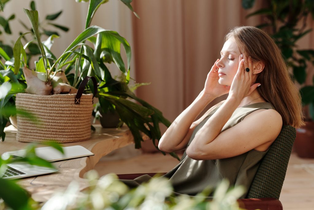 Woman sitting at a table with a laptop, holding her face in her hands, showing symptoms of iron deficiency anemia.