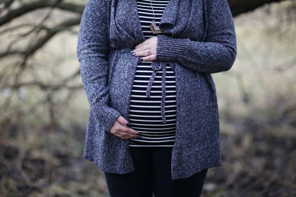 Pregnant woman standing outdoors, hands on her belly, highlighting the need for more iron to support baby’s oxygen supply.