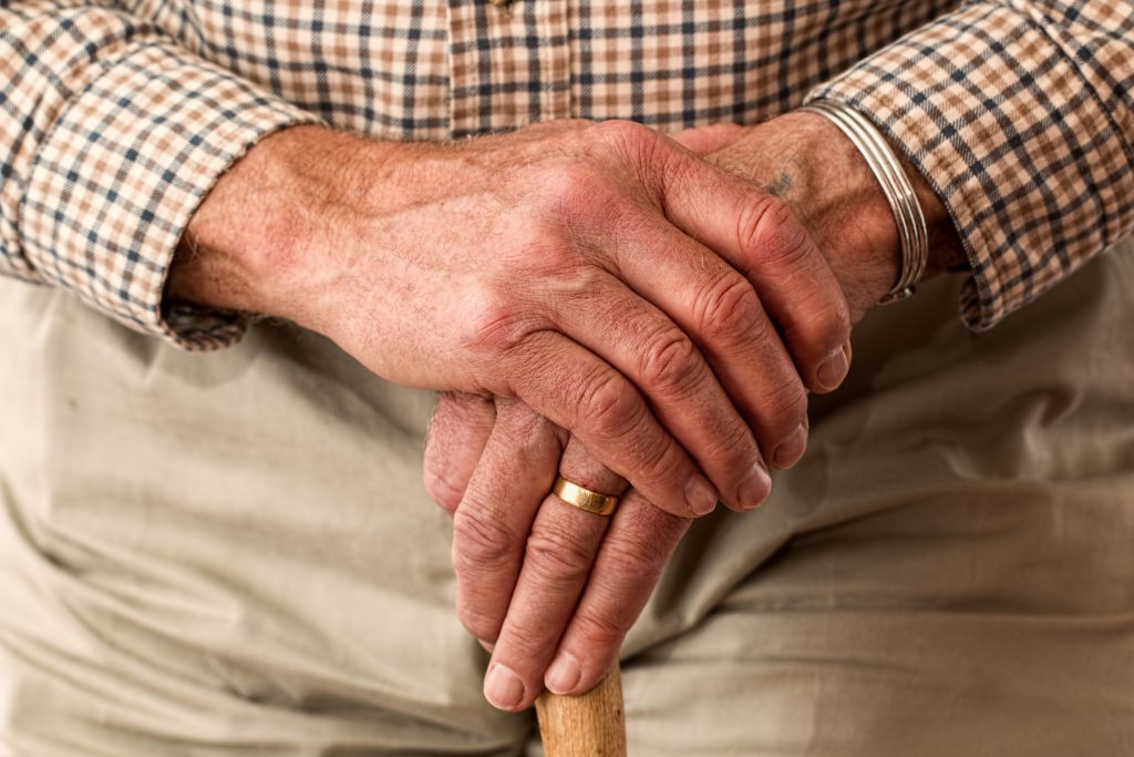 An elderly person gripping a walking stick, with a gold ring, showing an increased risk of Vitamin B12 deficiency.