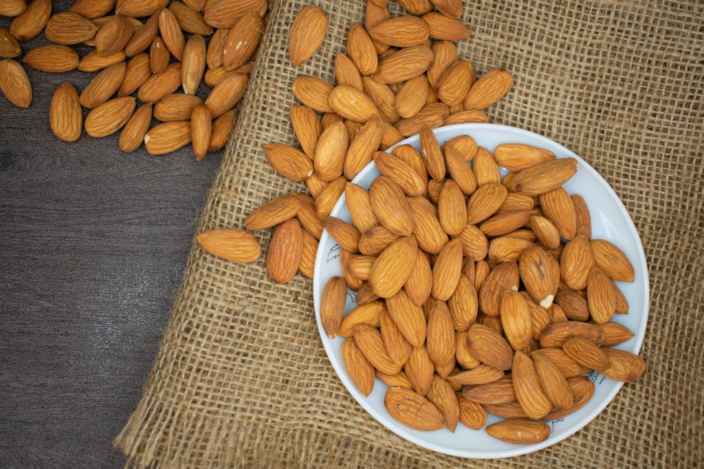 A bowl of fresh raw shelled almonds with some spilling onto a wooden board, delivering a serious fat-burning punch.