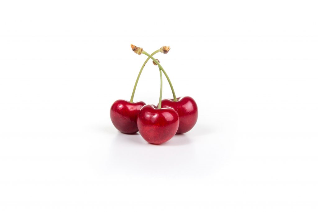 Three cherries with green stems on a white background, known to help reduce the risk of gout attacks in those with history.