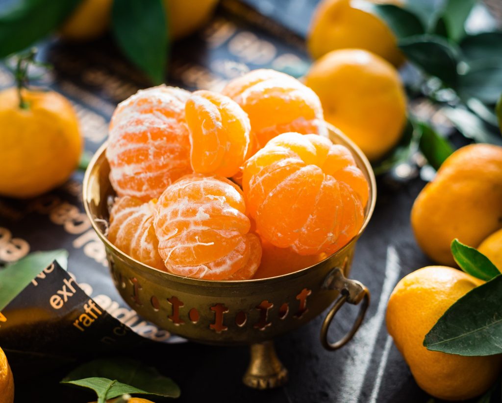 A bowl of peeled oranges with unpeeled ones scattered, rich in antioxidants that neutralize free radicals and protect cells.