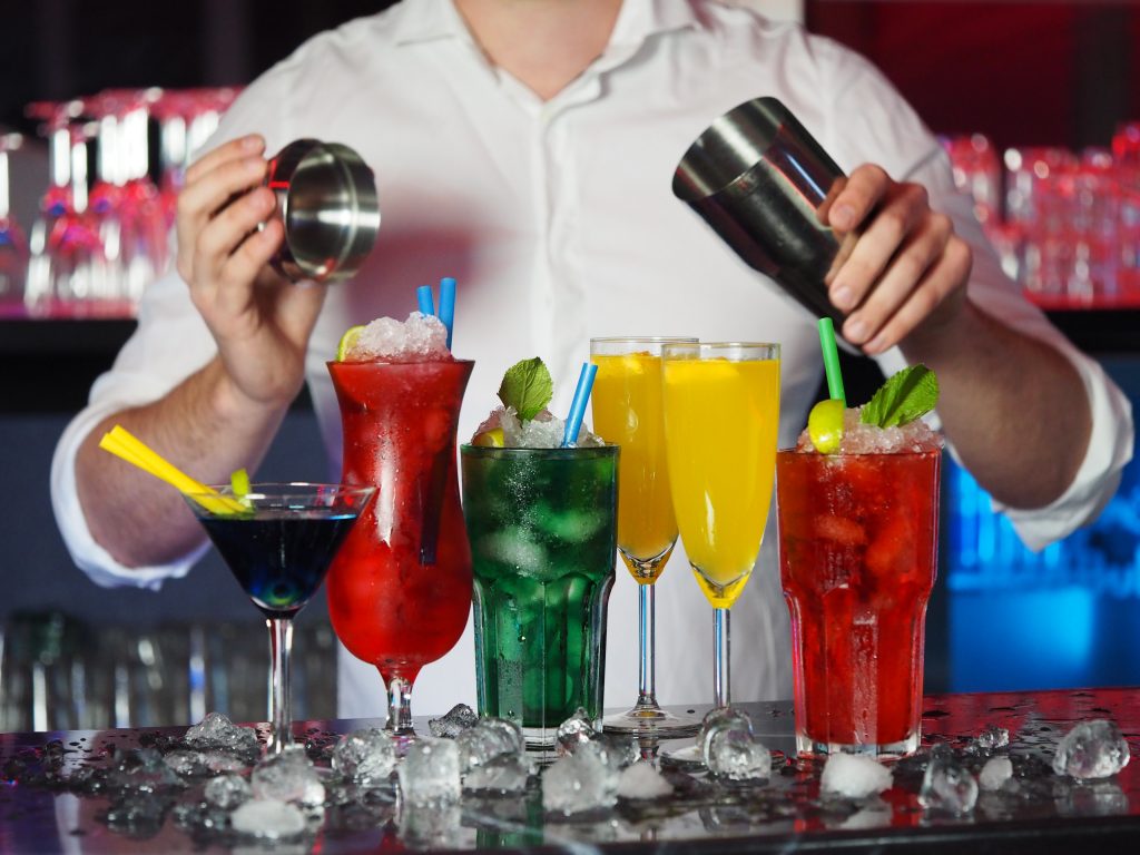 Bartender pouring drinks and colorful cocktails on ice, suggesting the benefits of limiting alcoholic beverages.