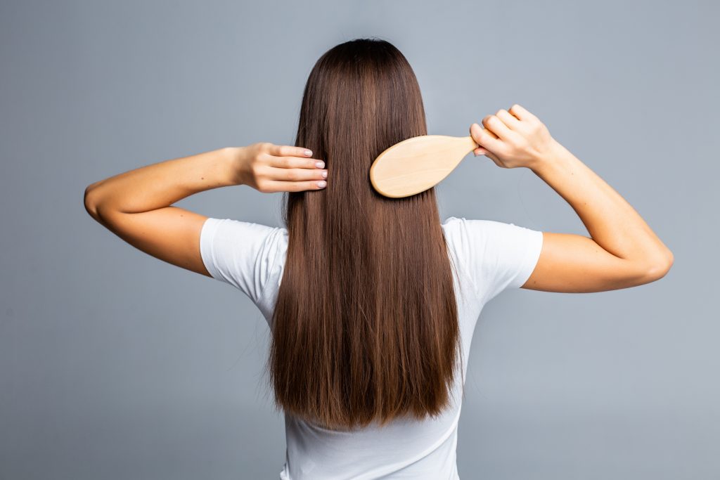 A woman with long brown hair brushing it with a wooden brush, supporting healthy hair, skin, and nails through Vitamin B12.