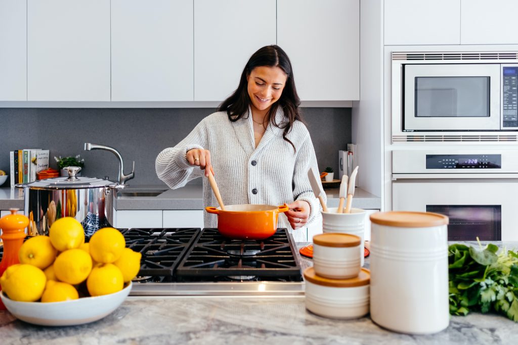 A woman happily cooking in a modern kitchen, using an orange pot to prepare healthy meals that support weight loss.