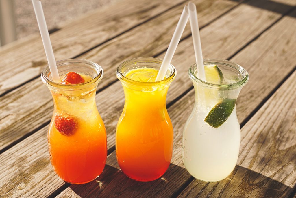 Colorful summer cocktails on a wooden table with straws, highlighting the need to avoid sugary beverages.
