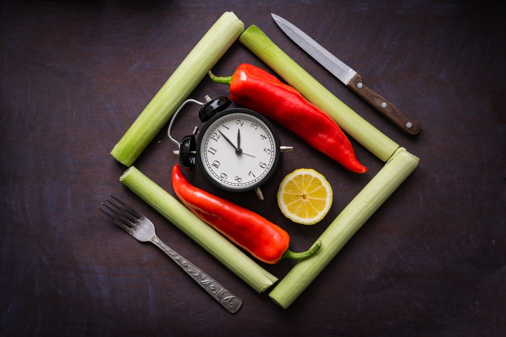A clock with peppers, leeks, lemon, and cutlery, symbolizing intermittent fasting's impact on hormones and weight reduction.
