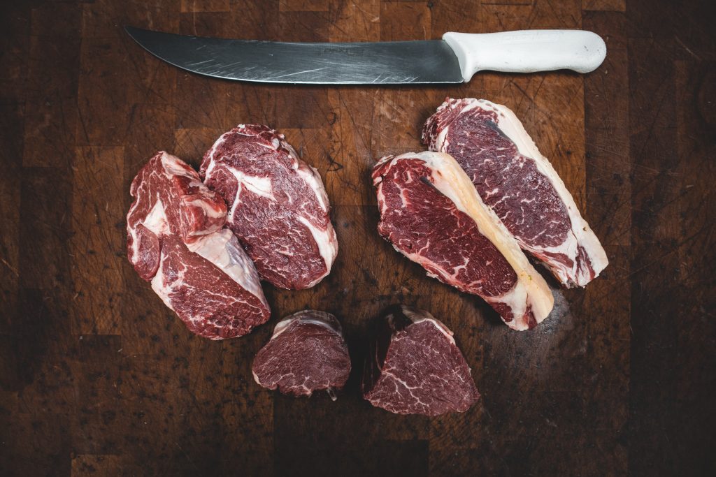 Raw meat cuts on a wooden surface with a large knife, rich in nutrients that help reduce tiredness and fatigue.