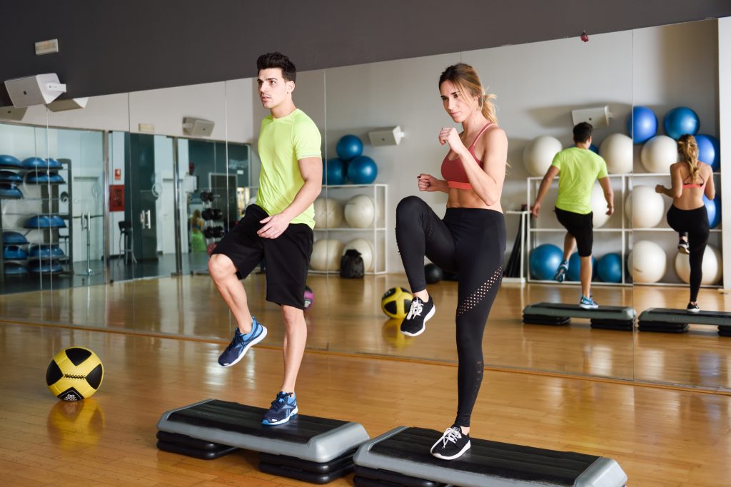 Two people performing aerobic exercises in a gym with fitness balls and equipment in the background, symbolizing a boost to physical and mental well-being.