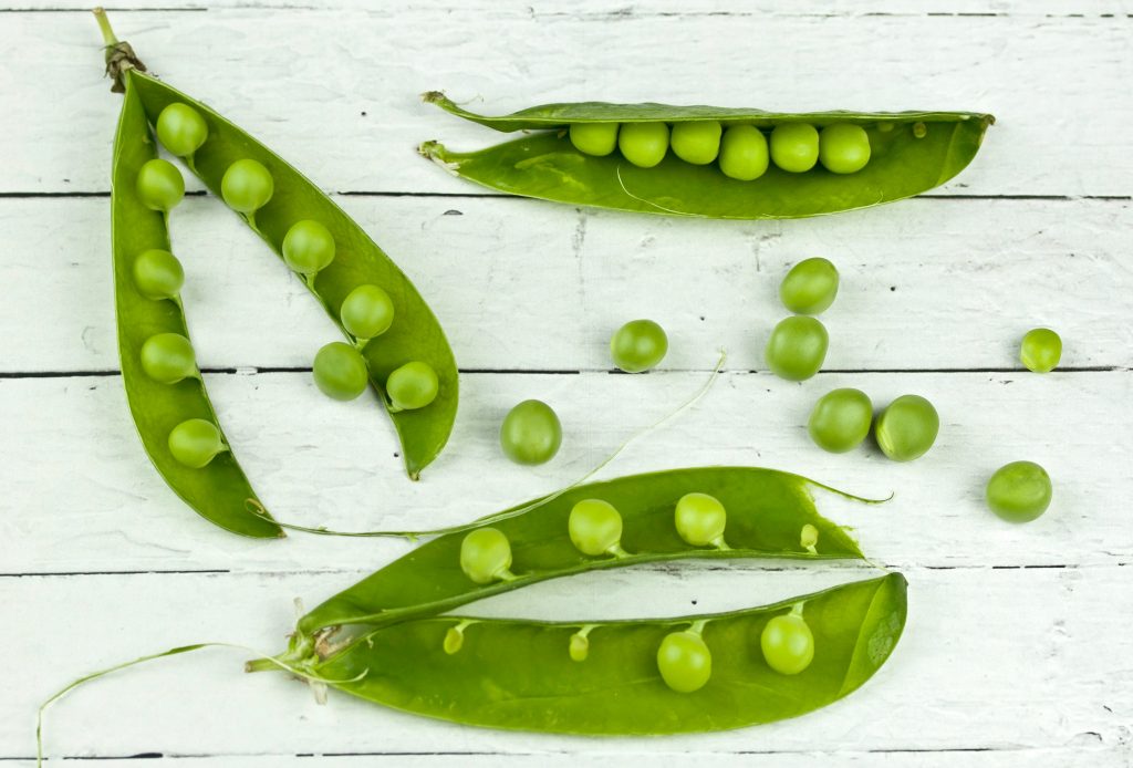 Peas in pods on a white surface, with some removed, representing the importance of vitamin B1 for brain and heart function.