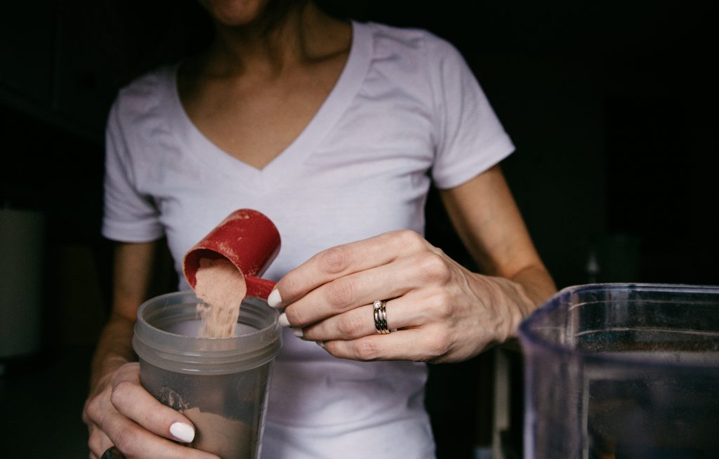 A person adding protein powder to a shaker bottle, a high-quality dairy protein that supports muscle mass growth.