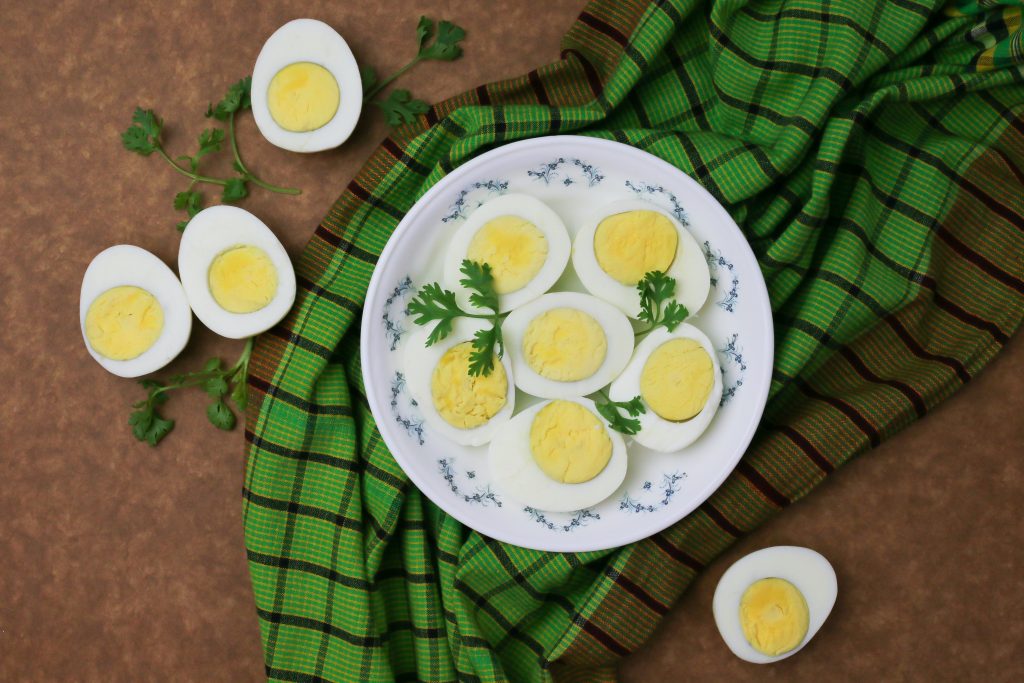 A plate of sliced hard-boiled eggs garnished with parsley, placed on a green checkered cloth, showcasing a healthy snack option for sudden hunger.