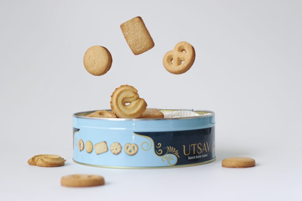 A blue tin of butter cookies surrounded by cookies in mid-air, reflecting the rapid energy spikes refined carbs can cause.