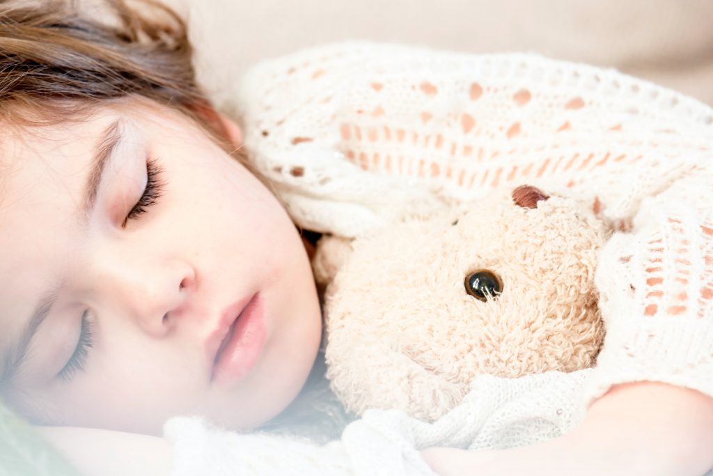A little girl peacefully sleeps with her teddy bear, highlighting the importance of rest for health.