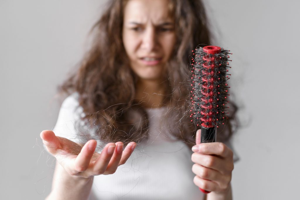Woman examining hair strands in her hand, worried about hair loss, a possible sign of thyroid hormone imbalance.