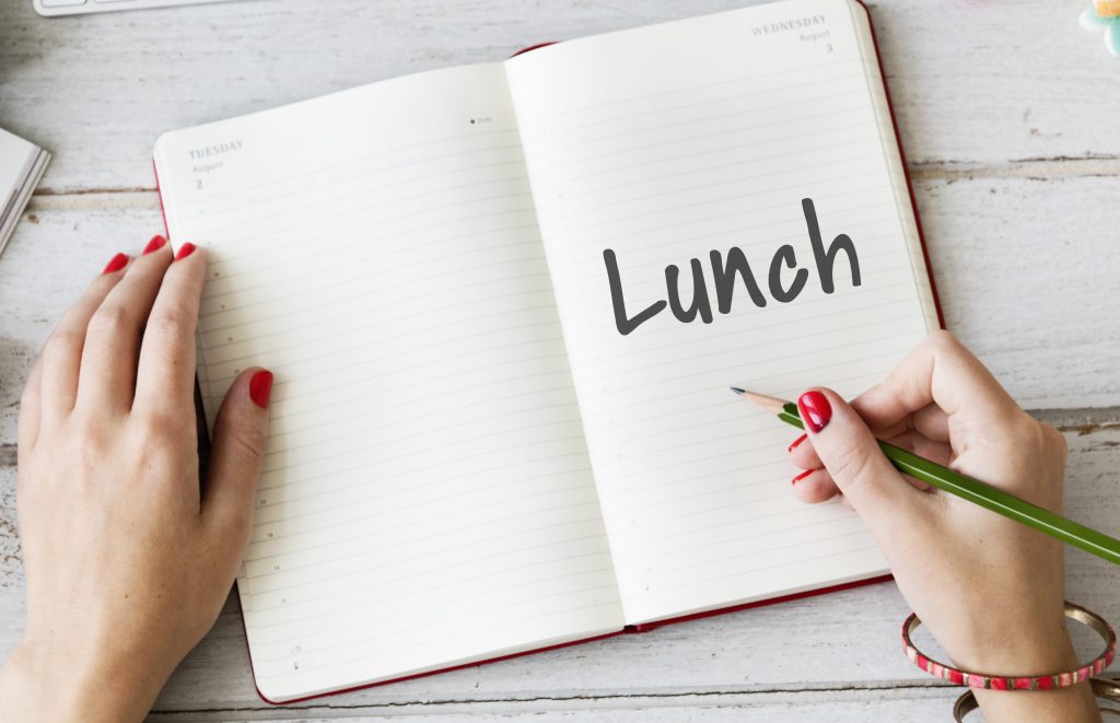 A person writing "Lunch" in a notebook with a green pencil, highlighting how excess calorie intake may cause weight gain.
