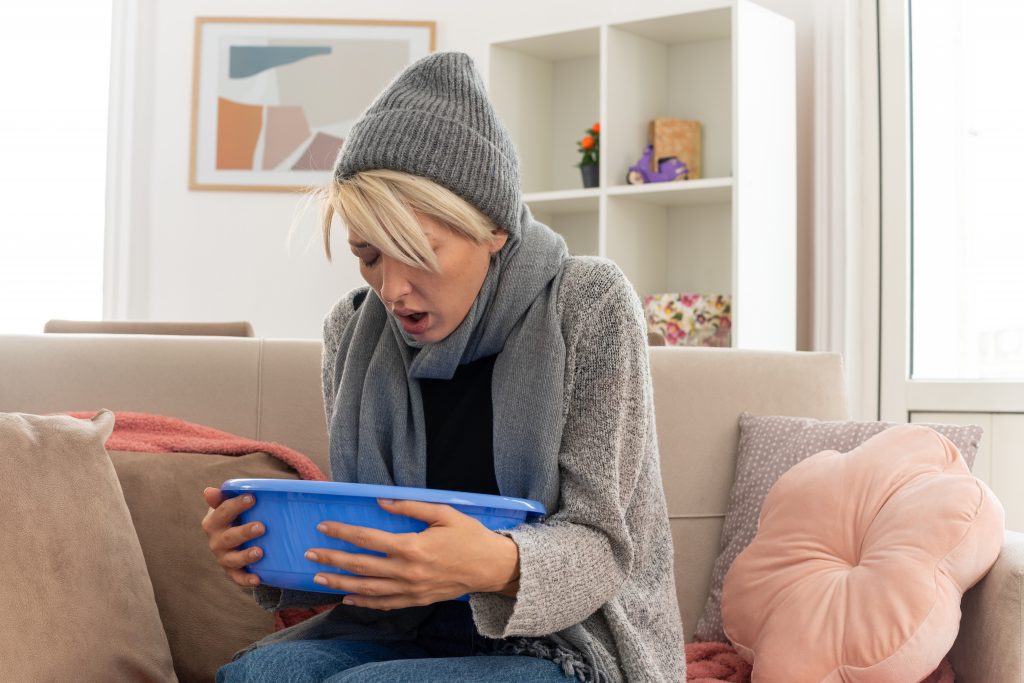 A woman in a woolen cap and sweater holding a blue tub, indicating nausea from excessive zinc supplementation.