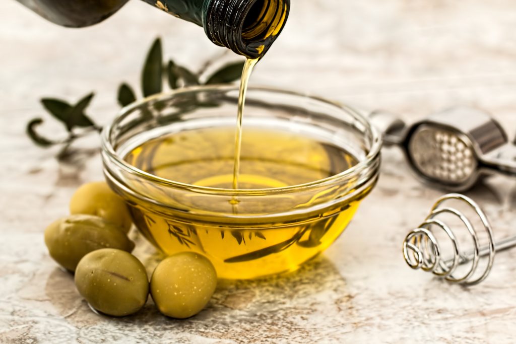 Pouring olive oil into a glass bowl, rich in Vitamin E, which acts as an antioxidant neutralizing free radicals.