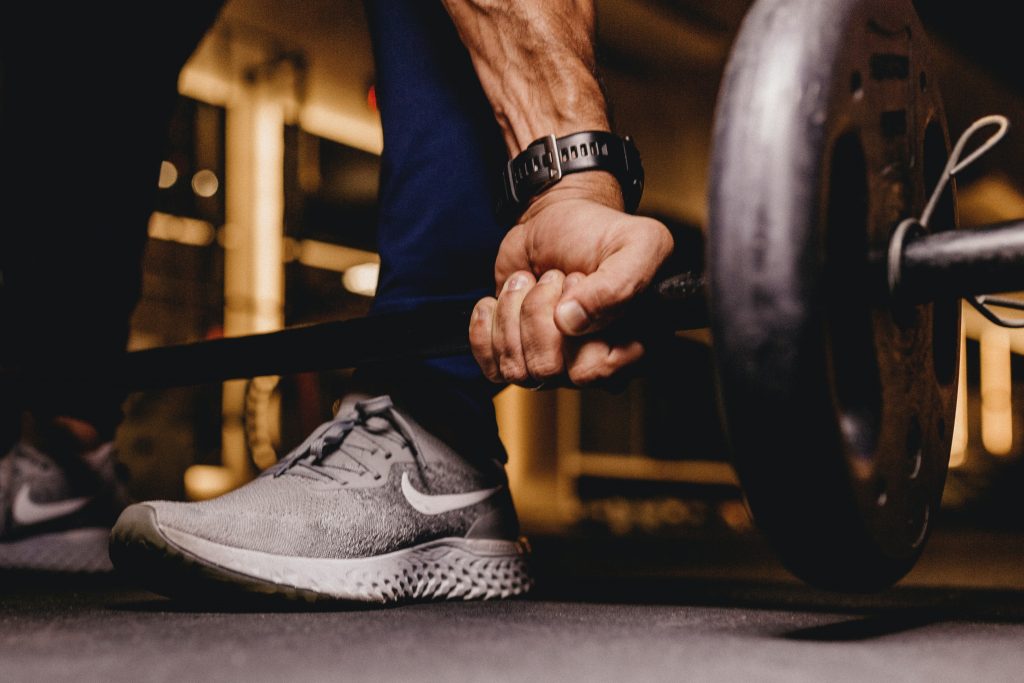 A person at the gym lifting heavy weights with a fitness tracker, showing how intense workouts help burn belly fat.