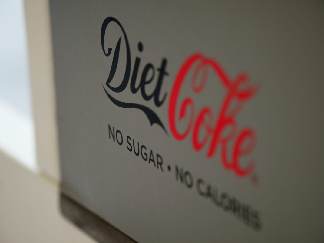 Close-up of Diet Coke packaging with 'No Sugar - No Calories' text, which may increase the risk of migraine headaches.