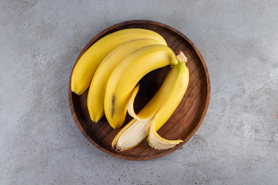 A wooden bowl with unpeeled bananas and one peeled banana, highlighting their role in lowering blood pressure and supporting heart health.