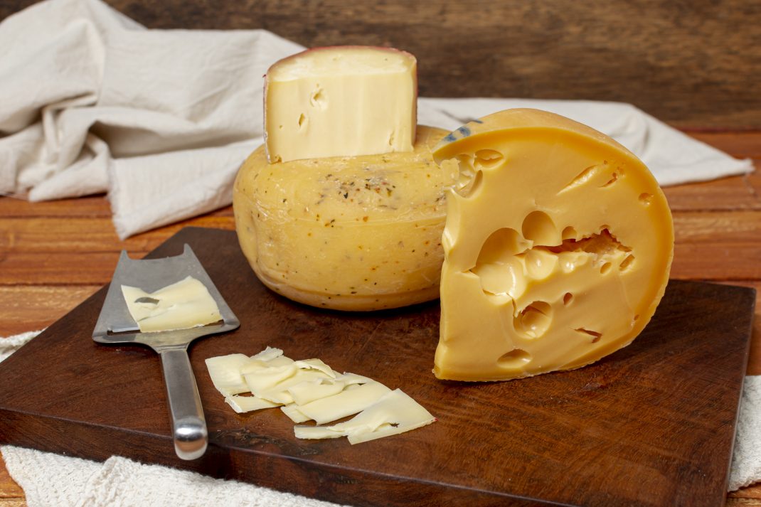 Cheese slices and knife on a board, containing substances that may trigger migraines.