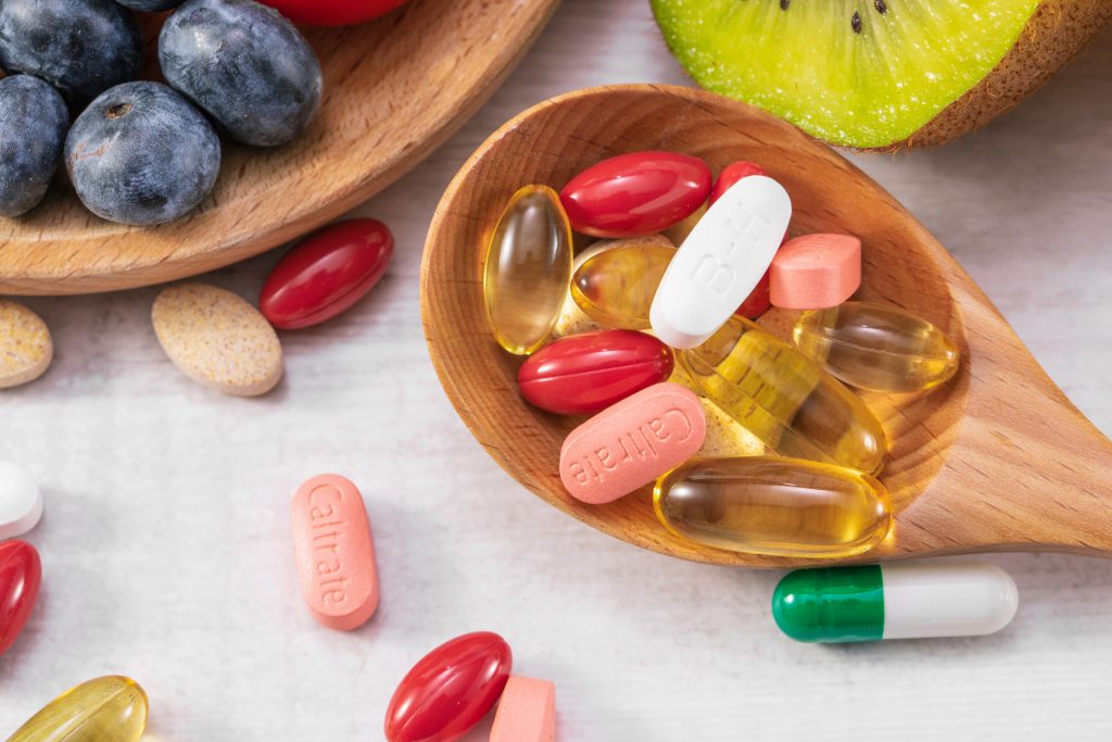 Close-up of fresh fruits and medicine on a wooden spoon, highlighting nutrients for bone health and the need for vitamin supplements.