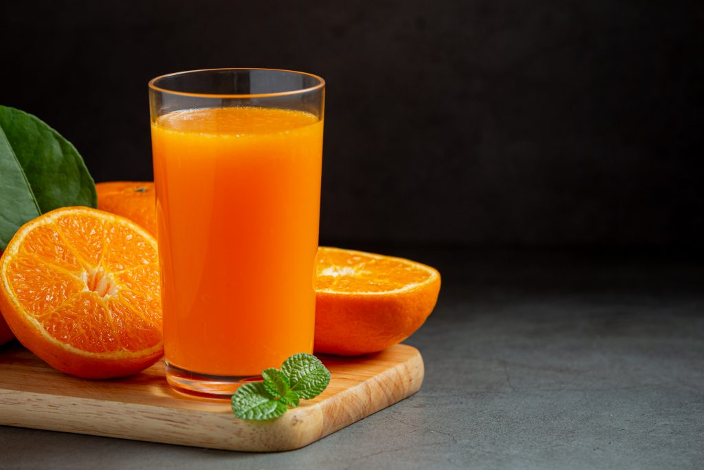 A glass of orange juice on a wooden board with fresh oranges and mint, a reminder to swap juice for fiber-rich whole fruits.