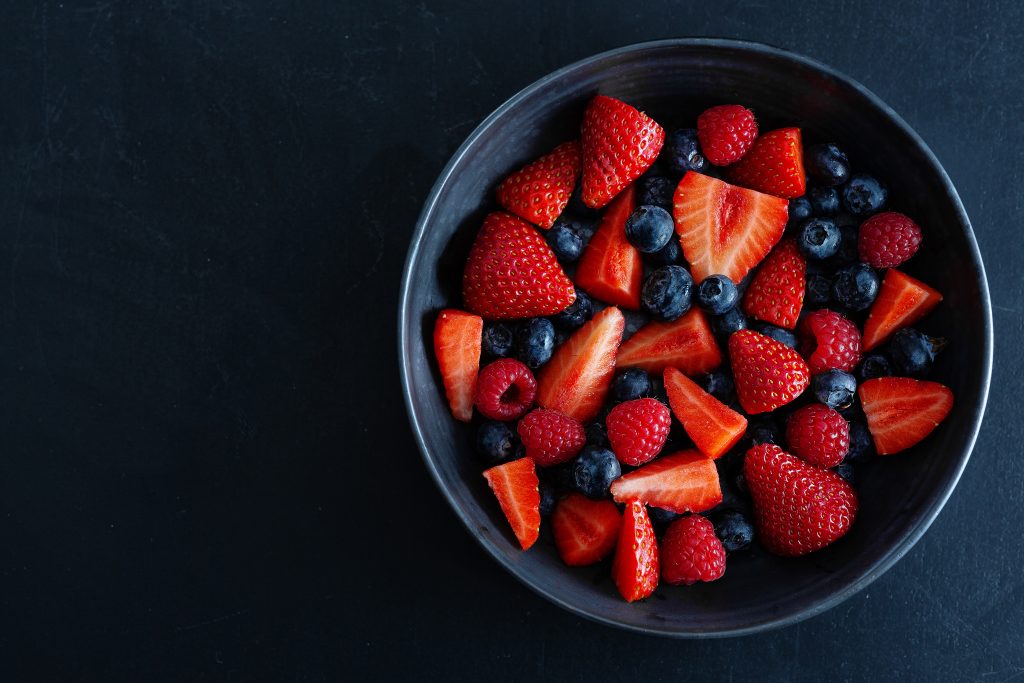 A bowl of strawberries, blueberries, and raspberries, helping to lower cholesterol and prevent heart disease.