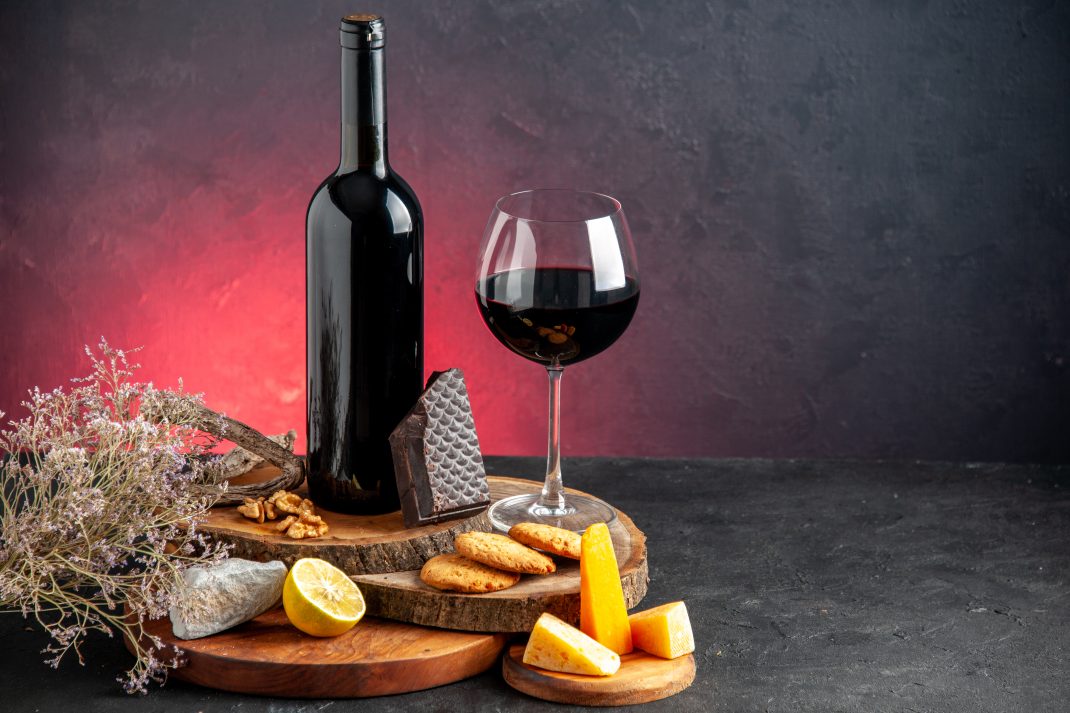 A glass and bottle of red wine, surrounded by snacks, could trigger a migraine attack due to alcoholic beverages.