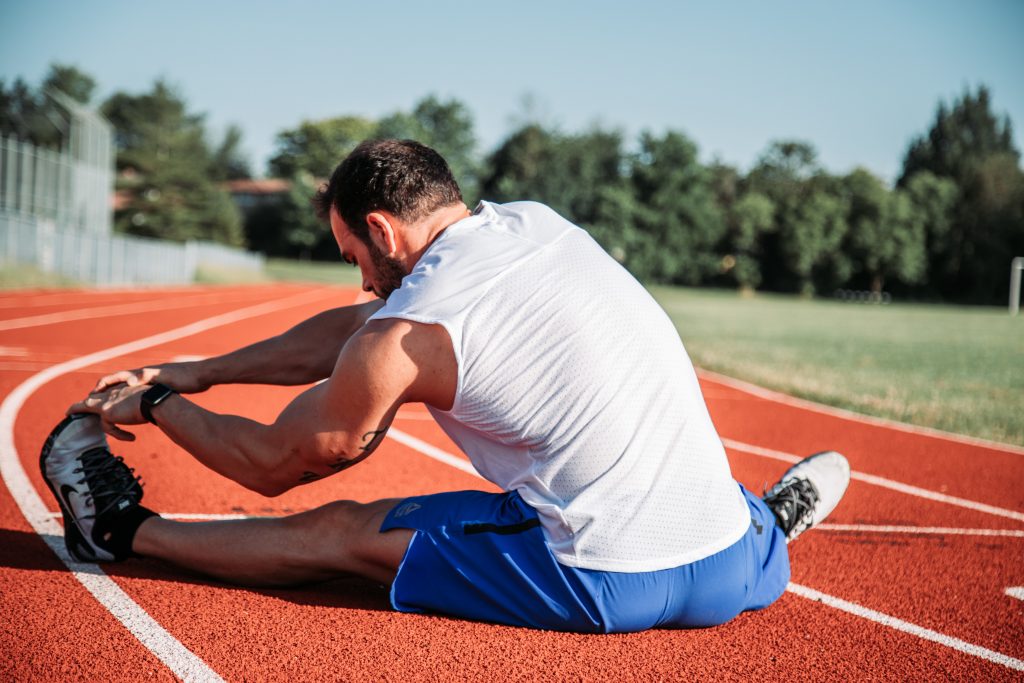 A man sitting on a track and stretching his legs, highlighting how regular stretching strengthens muscles and tendons.