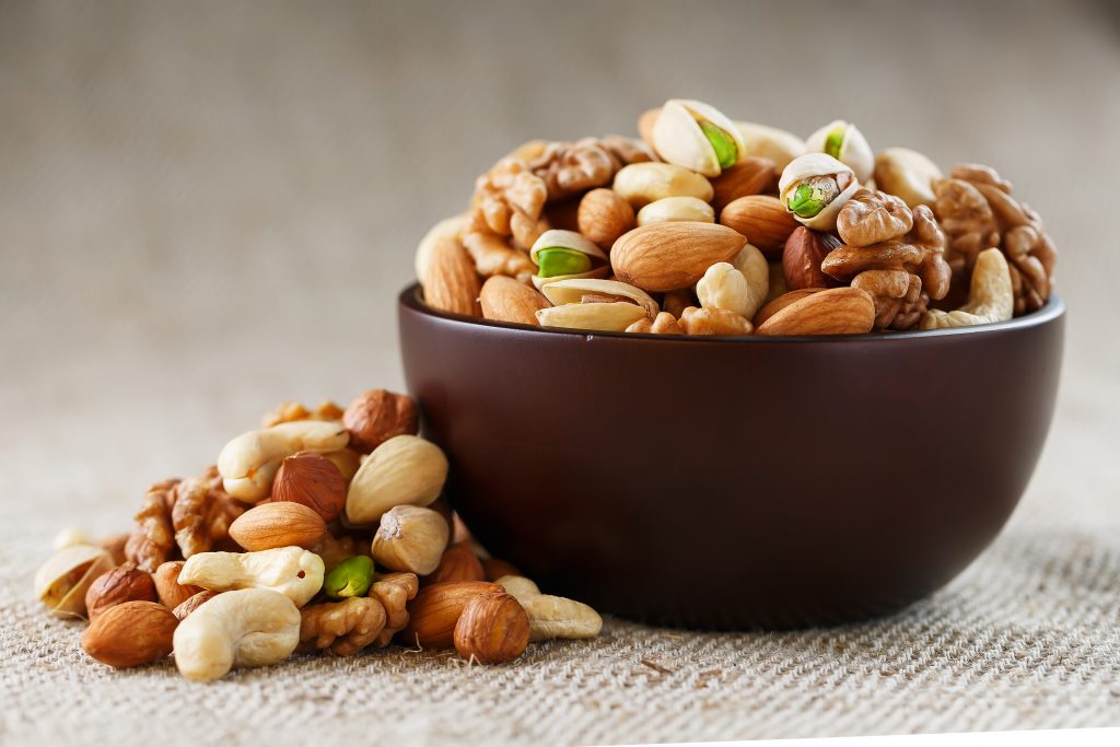 A brown bowl filled with mixed nuts like almonds, walnuts, pistachios, and cashews, highlighting healthy fats for flavor and satiety.