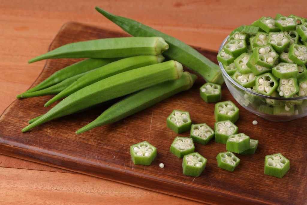 Close-up of fresh green okra, whole and sliced, in a bowl on a cutting board showcasing mucilage that helps lower cholesterol by binding during digestion.