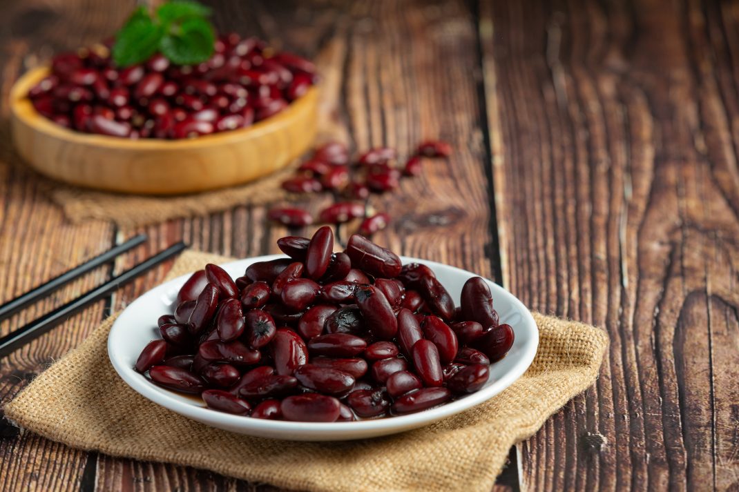 A bowl of cooked kidney beans with chopsticks and raw beans behind, highlighting benefits like better blood sugar control and lower colon cancer risk.