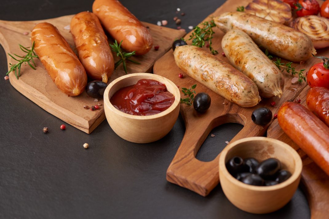 Grilled sausages with ketchup on a wooden board, may release nitric oxide and trigger migraines.