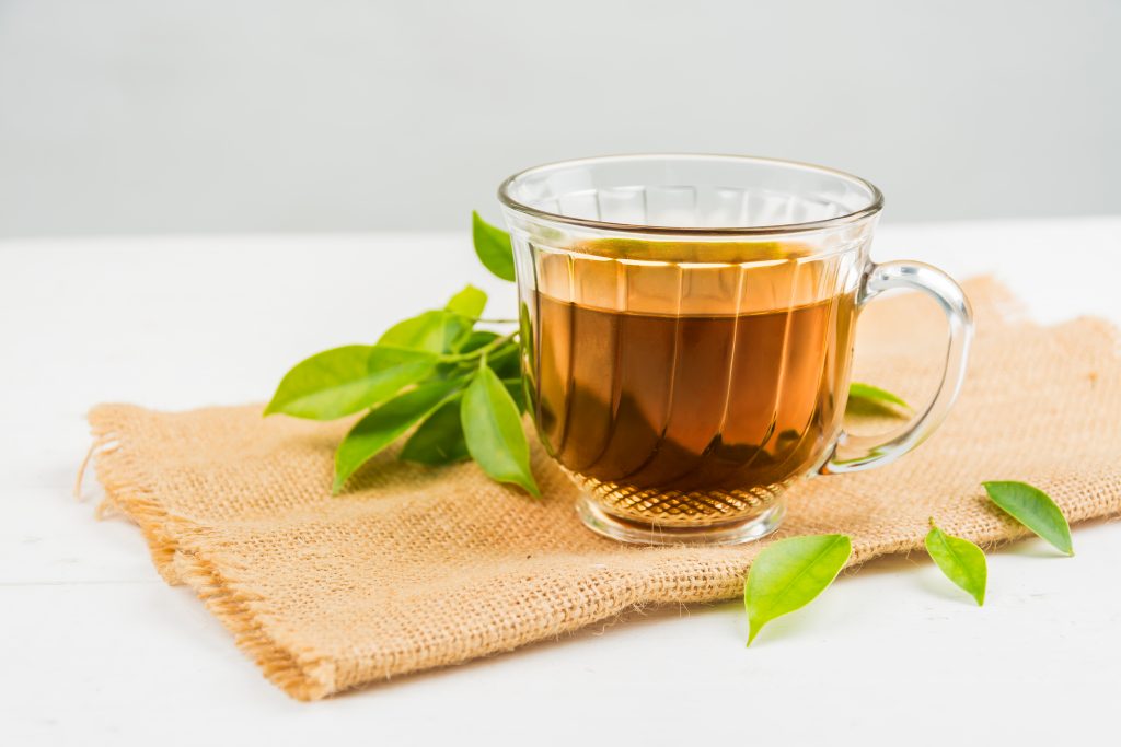 Green tea with fresh leaves on a burlap napkin, promoting healthy cholesterol levels and preventing blood clots.