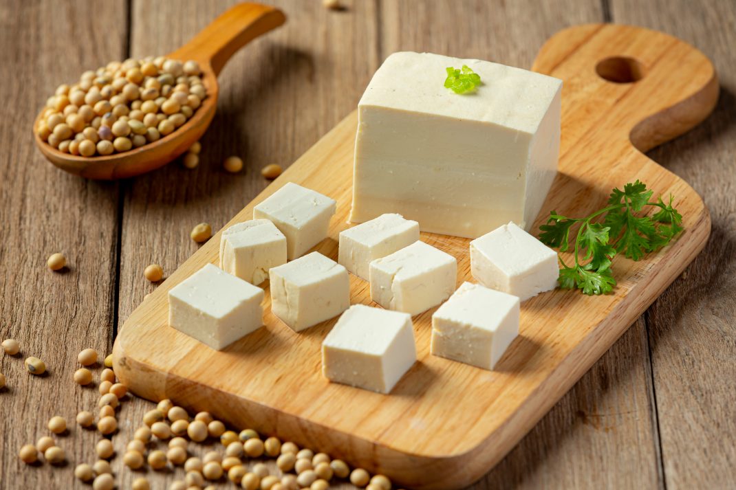 Tofu block and cubes on a wooden cutting board with soybeans, highlighting a vegetarian protein and magnesium source.