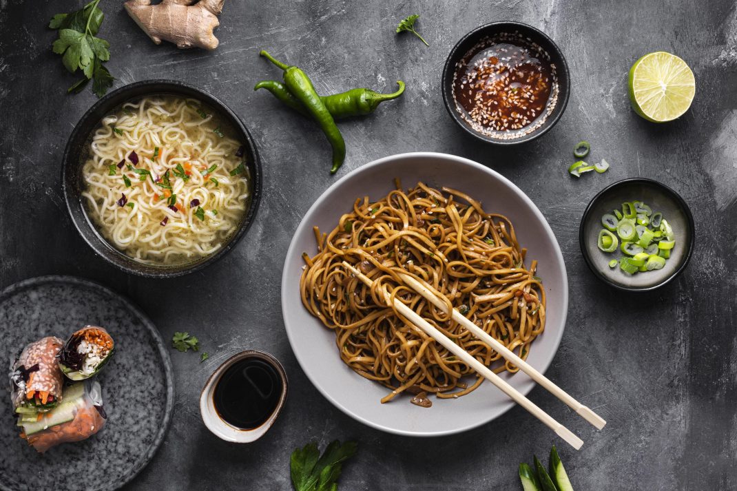 A dish of fried noodles with chopsticks, chili, sauce, and boiled noodles, possibly containing MSG that may cause migraines.