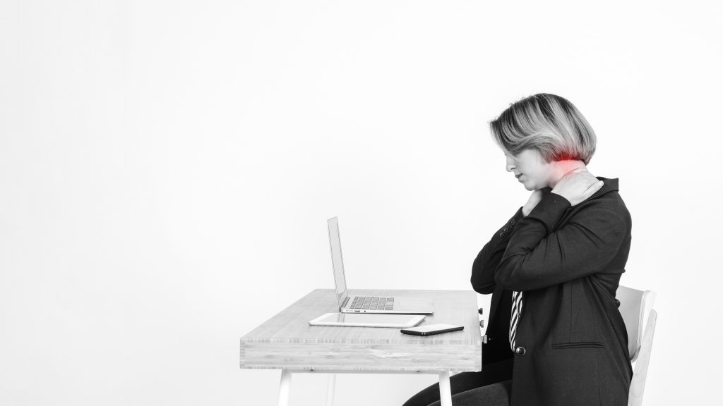 A professional woman working on her laptop, holding her neck in pain, illustrating the effects of bad posture.